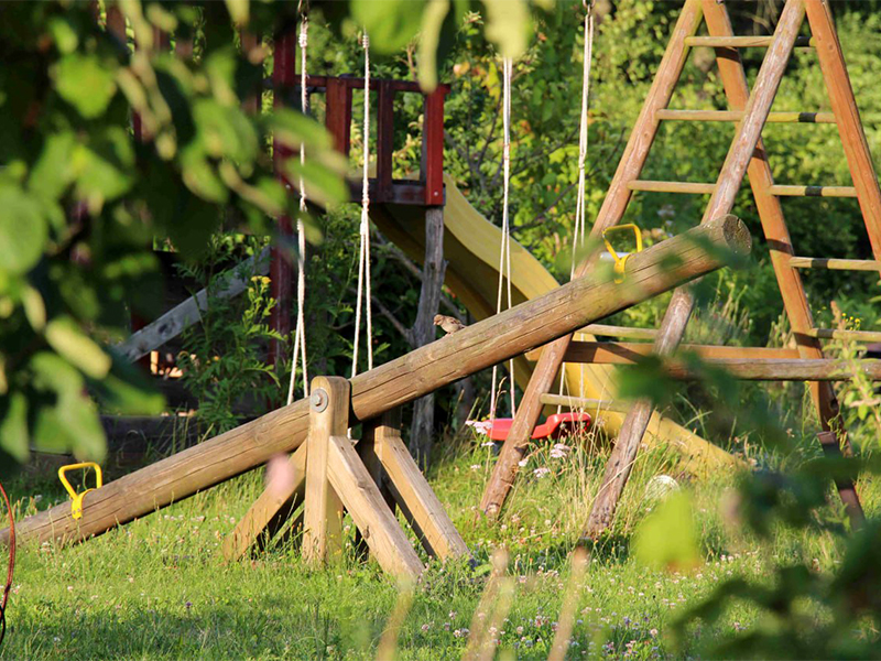 Dekoratives Foto eines Spielplatzes in der Siedlung Neumühlen. Ein Vogel sitzt auf einer Wippe.