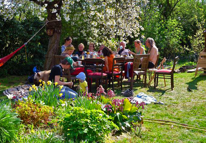 Foto des Gartens in Stedorf, an einem großen Tisch sitzen die Bewohner und essen. Es ist sonnig und die Bäume blühen.